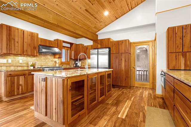 kitchen featuring under cabinet range hood, brown cabinets, decorative backsplash, and freestanding refrigerator