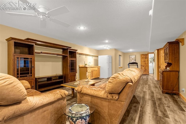 living area with light wood-style floors, a textured ceiling, baseboards, and a ceiling fan