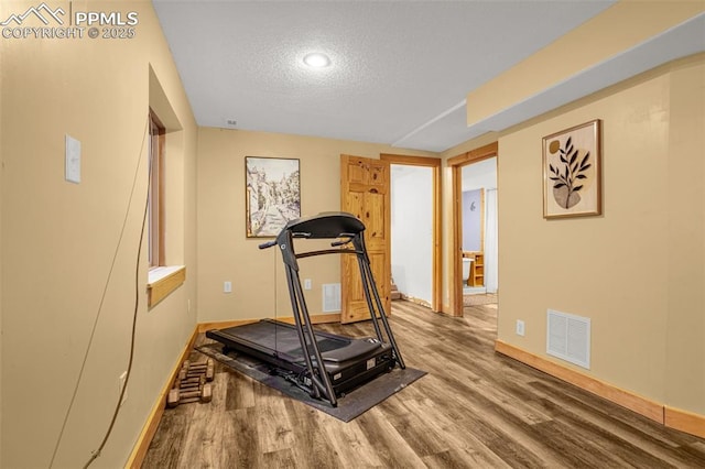 exercise room featuring a textured ceiling, wood finished floors, visible vents, and baseboards