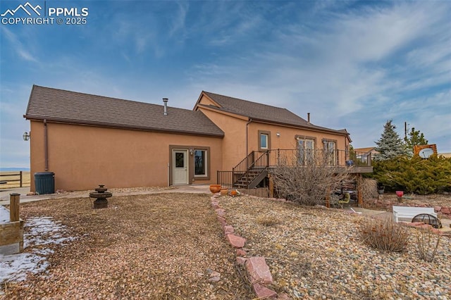 rear view of property featuring stairs, a wooden deck, and stucco siding