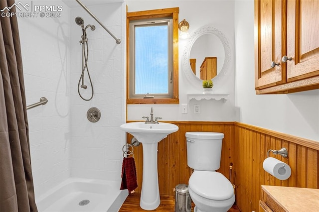 bathroom featuring wood walls, wainscoting, a tile shower, and toilet