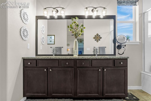 bathroom with baseboards, a tile shower, a sink, and double vanity