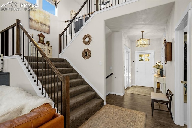 foyer with a towering ceiling, an inviting chandelier, wood finished floors, baseboards, and stairs