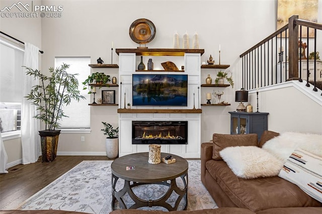 living room with a glass covered fireplace, stairway, baseboards, and wood finished floors