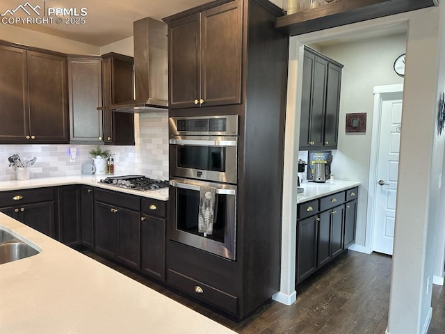 kitchen with tasteful backsplash, dark wood-style flooring, stainless steel appliances, light countertops, and wall chimney range hood