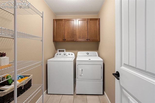 clothes washing area with cabinet space, light tile patterned floors, baseboards, and washing machine and clothes dryer