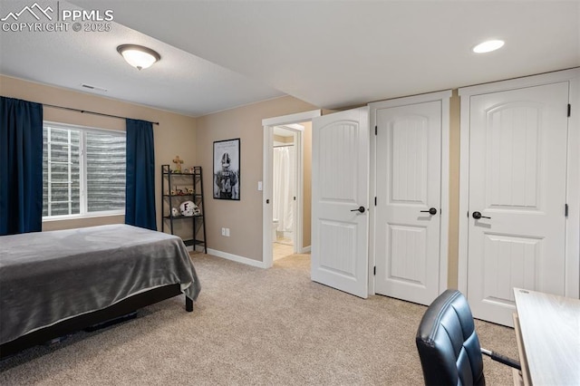 bedroom with light carpet, baseboards, visible vents, ensuite bathroom, and two closets