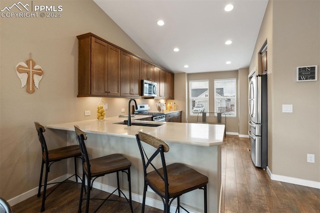 kitchen with a peninsula, a sink, light countertops, appliances with stainless steel finishes, and dark wood finished floors