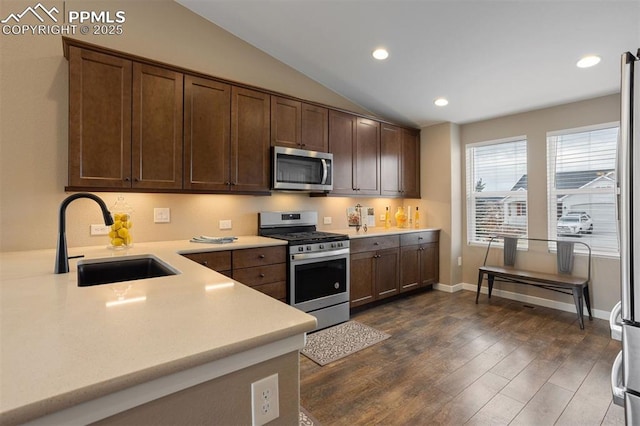 kitchen featuring a sink, vaulted ceiling, light countertops, appliances with stainless steel finishes, and dark wood finished floors