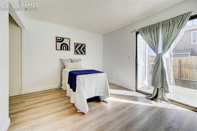 bedroom featuring access to outside, wood finished floors, baseboards, and a textured ceiling