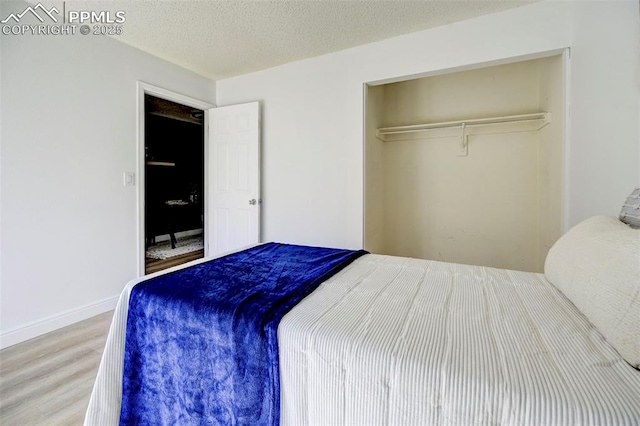 bedroom featuring a closet, a textured ceiling, baseboards, and wood finished floors