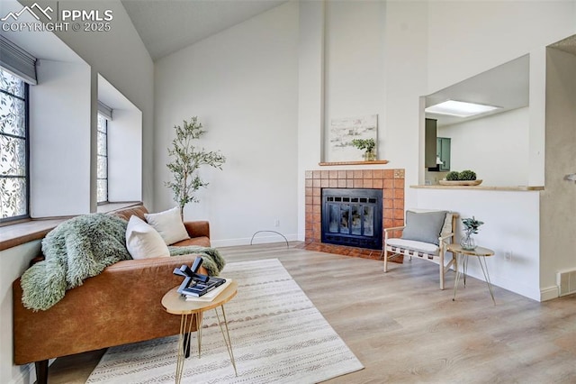 living room featuring wood finished floors, baseboards, visible vents, high vaulted ceiling, and a tiled fireplace