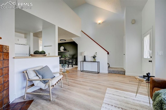 interior space with stairway, baseboards, light wood-type flooring, and high vaulted ceiling