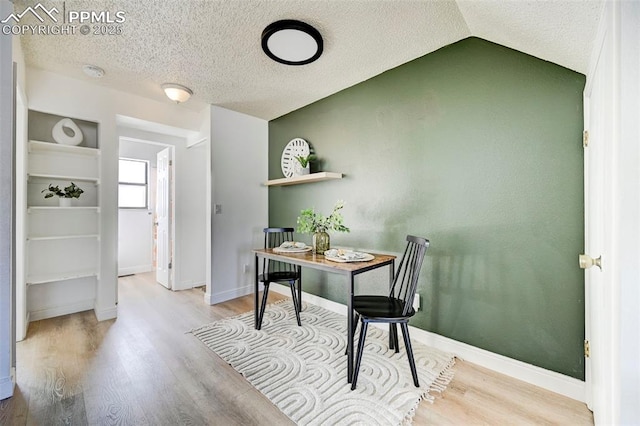 office space with light wood-style flooring, a textured ceiling, baseboards, and lofted ceiling