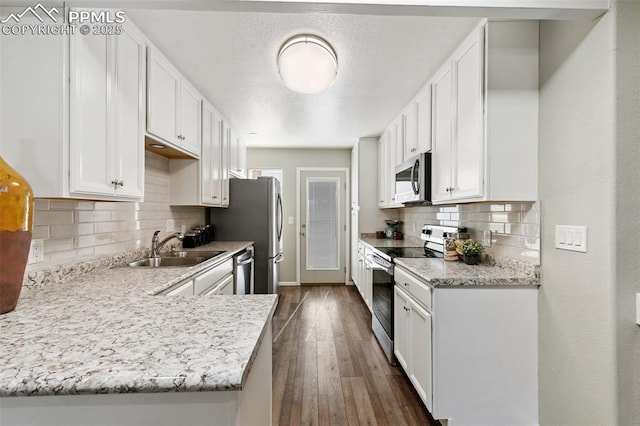 kitchen with a peninsula, a sink, white cabinetry, appliances with stainless steel finishes, and dark wood finished floors