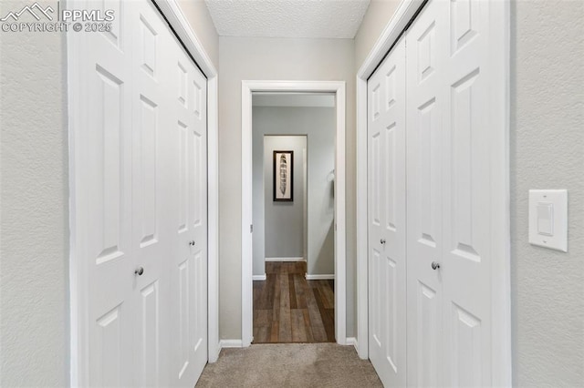 hallway featuring a textured ceiling, carpet floors, a textured wall, and baseboards