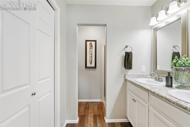 bathroom with a sink, double vanity, wood finished floors, and baseboards