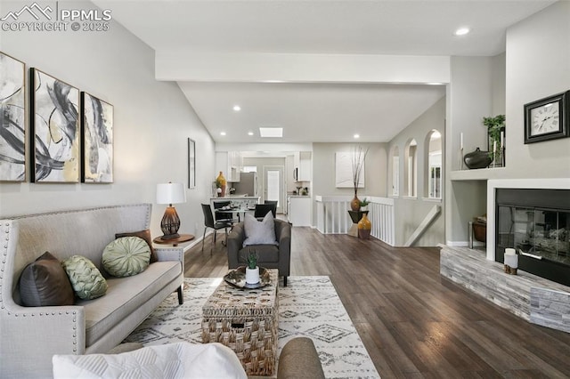 living room with a glass covered fireplace, wood finished floors, beam ceiling, and recessed lighting