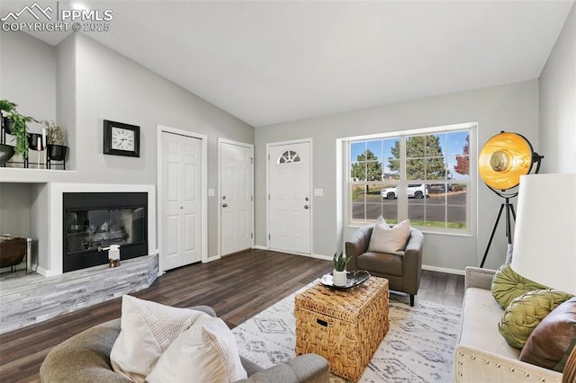 living room featuring lofted ceiling, baseboards, wood finished floors, and a glass covered fireplace