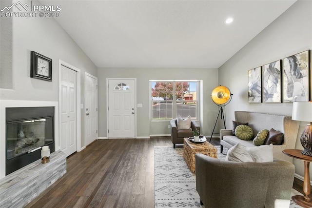 living area with lofted ceiling, dark wood-style flooring, a glass covered fireplace, and baseboards