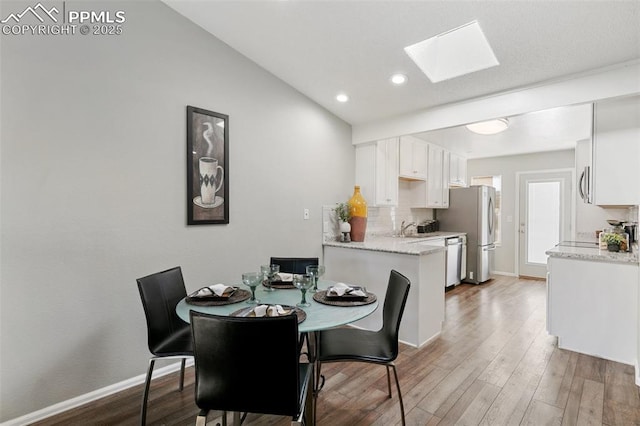dining area featuring a skylight, baseboards, wood finished floors, and recessed lighting