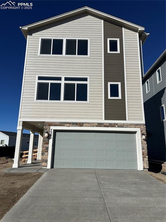 view of front of home with a garage, stone siding, and concrete driveway