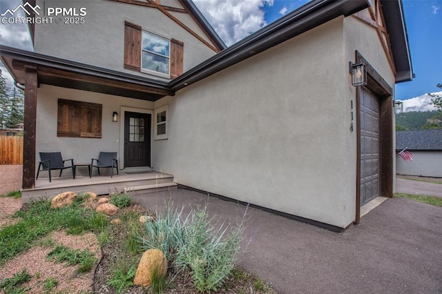 rear view of property featuring an attached garage, fence, a porch, and stucco siding