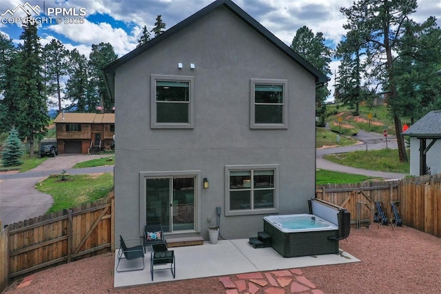 rear view of property with a fenced backyard, a patio, a hot tub, and stucco siding