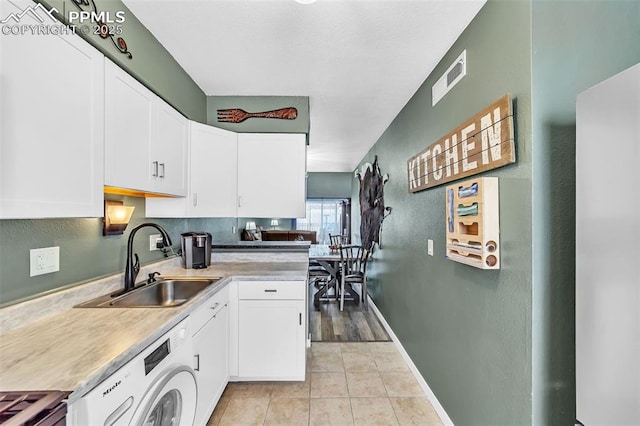 kitchen with washer / dryer, white cabinets, a sink, and light tile patterned flooring