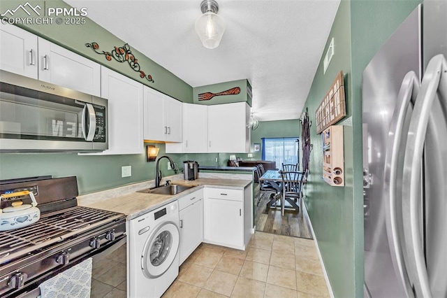 kitchen featuring light tile patterned floors, washer / clothes dryer, appliances with stainless steel finishes, white cabinetry, and a sink