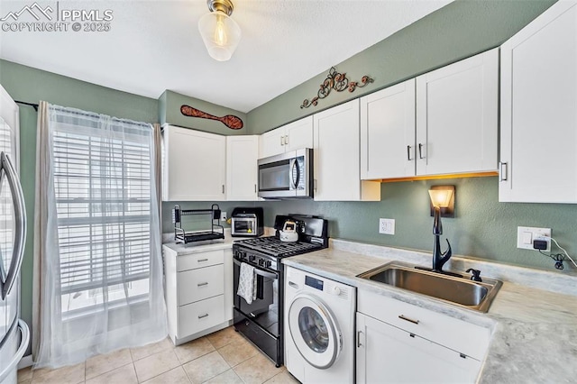 kitchen featuring light tile patterned floors, a sink, light countertops, appliances with stainless steel finishes, and washer / clothes dryer