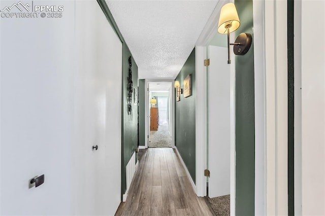 hallway with a textured ceiling, baseboards, and wood finished floors