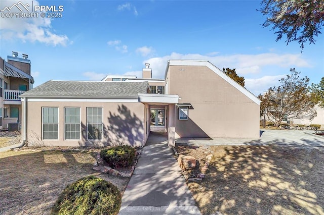 view of front of property featuring a shingled roof, a chimney, central AC, and stucco siding