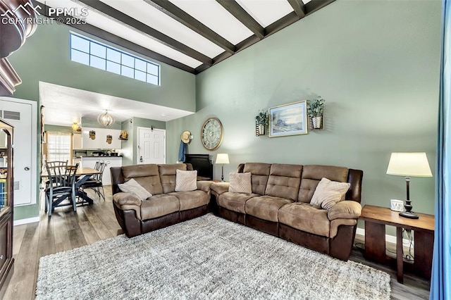 living room with beam ceiling, a high ceiling, baseboards, and wood finished floors