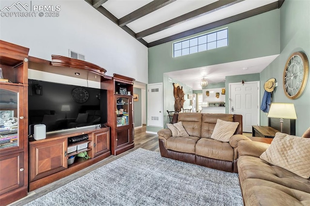 living area featuring visible vents, beamed ceiling, a high ceiling, and wood finished floors