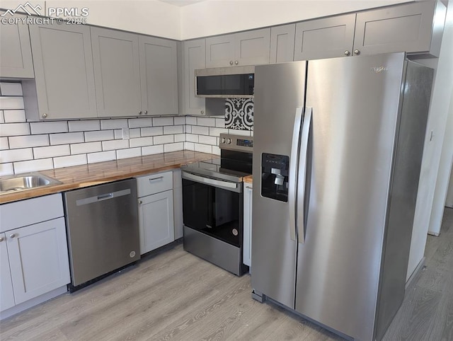 kitchen featuring light wood finished floors, tasteful backsplash, gray cabinetry, butcher block countertops, and stainless steel appliances