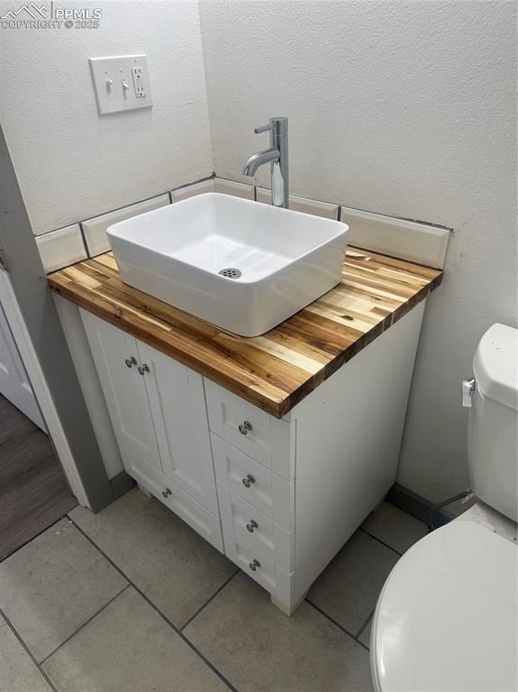 half bathroom featuring tile patterned flooring, toilet, vanity, and a textured wall