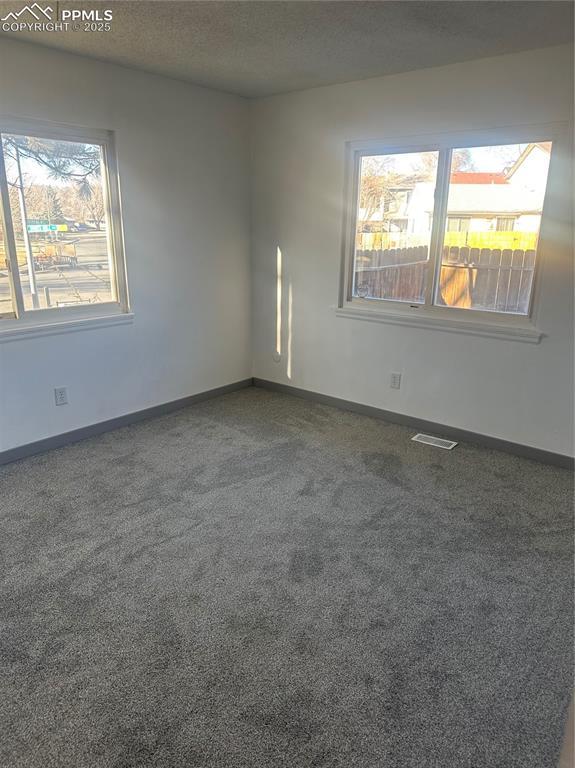 carpeted spare room featuring baseboards, visible vents, and a textured ceiling