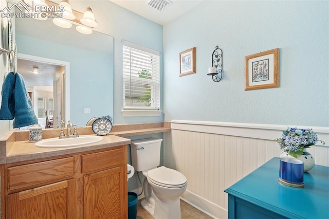 half bath featuring toilet, a wainscoted wall, visible vents, and vanity