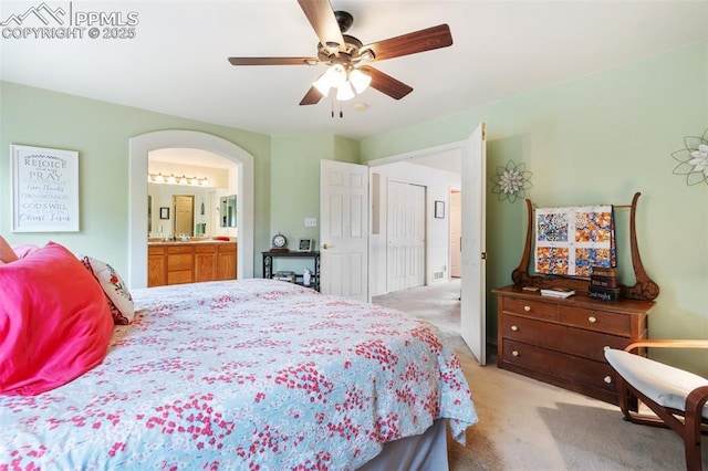 bedroom featuring light carpet, ceiling fan, arched walkways, and connected bathroom