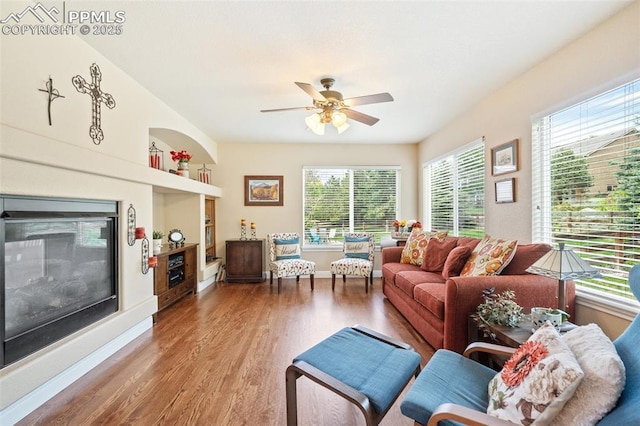 living room with a glass covered fireplace, ceiling fan, baseboards, and wood finished floors