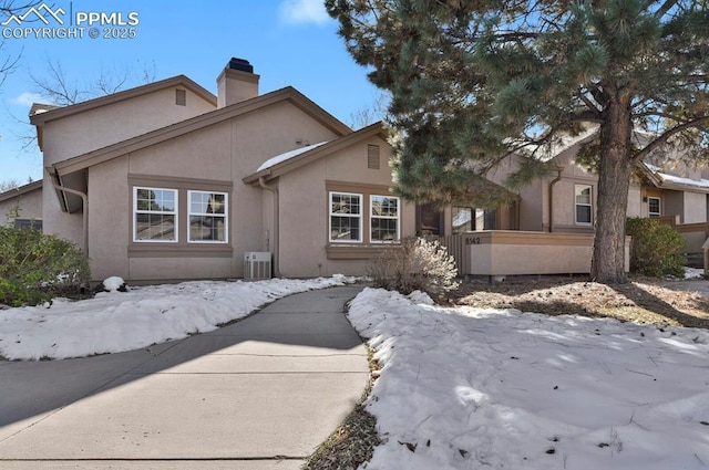 view of front of property featuring central AC unit, a chimney, and stucco siding