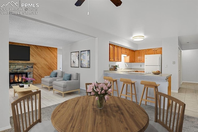 dining area featuring wooden walls, baseboards, a ceiling fan, a textured ceiling, and a fireplace