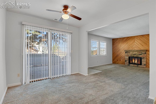 unfurnished living room with wooden walls, visible vents, a textured ceiling, a stone fireplace, and carpet floors