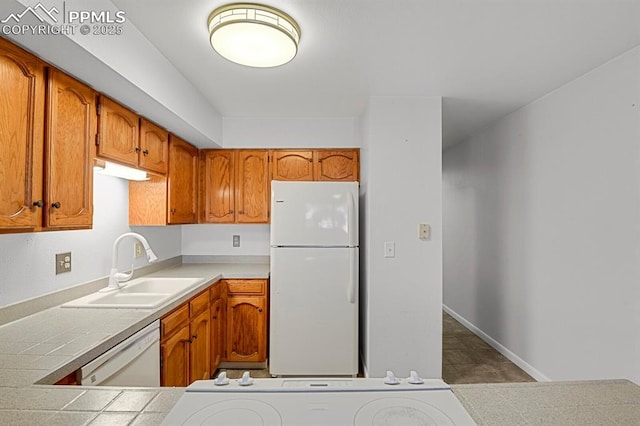 kitchen with white appliances, brown cabinetry, a sink, and baseboards