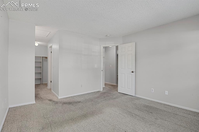 unfurnished room with a textured ceiling, carpet, attic access, and baseboards