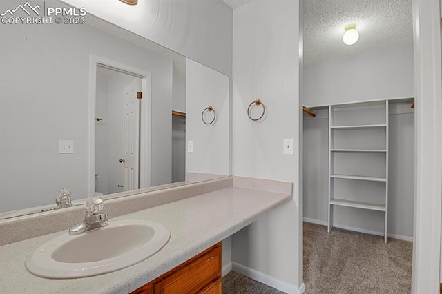 bathroom with baseboards, a textured ceiling, vanity, and a spacious closet