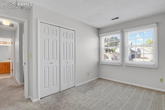 unfurnished bedroom featuring carpet floors, a closet, visible vents, a textured ceiling, and baseboards