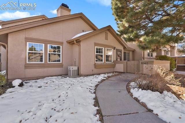 exterior space featuring central AC, a fenced front yard, a chimney, and stucco siding