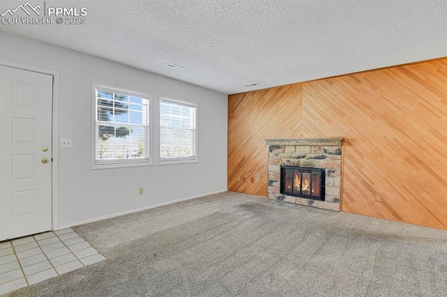 unfurnished living room featuring a textured ceiling, a stone fireplace, wood walls, and carpet flooring